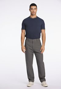 Chemise à manches courtes marine avec des accents verts, associée à un pantalon gris et des baskets blanches, présentant un design droit.