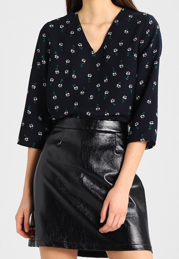 Mujer que lleva una blusa negra con flores y cuello en V, de mangas tres cuartos, metida dentro de una minifalda de cuero negro brillante.