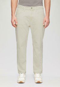 Jasno beżowe spodnie o prostym kroju, wykonane z teksturowanej tkaniny. Posiadają kieszenie z przodu i zapięcie na guzik, połączone z białymi trampkami.