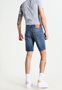 Jeansshorts i medelblått med rak skärning och fransad nederkant. Bärs med en gråmönstrad t-shirt och vita sneakers.