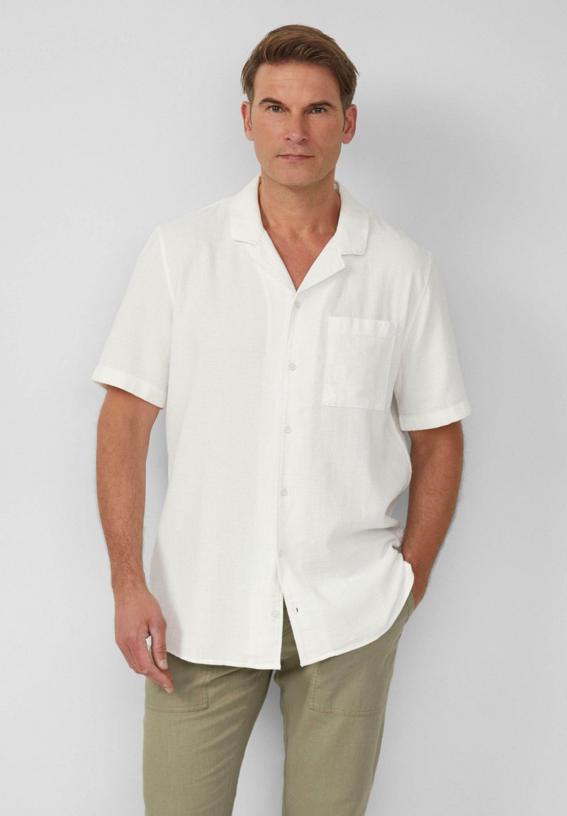 Chemise blanche à manches courtes avec une poche du côté gauche. Fabriquée dans un tissu texturé, elle présente un col décontracté et un ourlet droit.