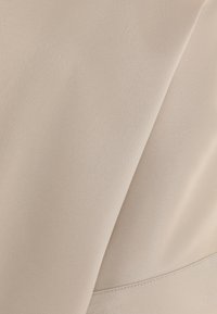 Vaalea kangas, jossa on sileä rakenne ja päällekkäisiä taitoksia sekä näkyviä saumanompeluja reunassa.