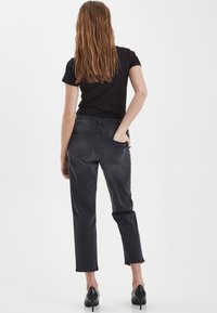 Haut noir côtelé associé à un jean gris droit taille haute, avec deux poches arrière et des poignets retroussés, porté avec des talons noirs.