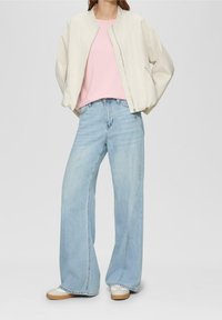 Jasny bomber na różowej koszulce, w połączeniu z szerokimi jasnoniebieskimi dżinsami i beżowymi trampkami. Gładkie tekstury, swobodny styl.