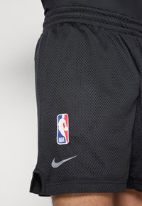 Pantalones cortos de baloncesto de malla negra con el logo de Nike y un parche del logo de la NBA con acentos en rojo, blanco y azul.