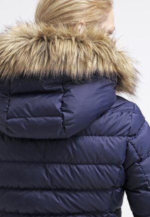Padded navy jacket featuring a detachable fur-lined hood, quilted design, and smooth texture. Back view shows fur accent around the collar.