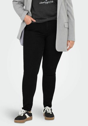 Black skinny jeans with a smooth texture, paired with a graphic charcoal t-shirt and a light gray pinstripe blazer. Black and white sneakers.