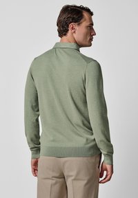 Grüner Strickpullover mit spitzem Kragen und langen Ärmeln. Gerippte Bündchen an Ärmeln und Saum. Glatte Textur, figurbetontes Design, minimalistische Details.