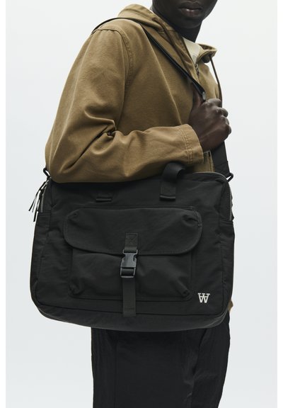 Sac messager en nylon noir avec rabat avant et boucle, doté d'une poche latérale zippée et d'un accent logo. Porté sur l'épaule.