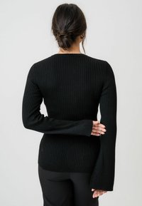 Schwarzer, gerippter Pullover mit langen Ärmeln, figurbetoneter Passform, rundem Ausschnitt und ausgestellten Bündchen. Der Stoff fühlt sich weich und dehnbar an.