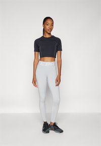 Svart crop-top med korte ermer, lysegrå høytlivede leggings med "NIKE PRO" elastikk i livet, fullført med svarte treningssko.
