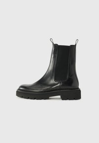 Bottines noires en cuir avec panneaux élastiques sur les côtés, bout rond et semelle en caoutchouc épaisse avec un motif de bande de roulement strié. Tirants pour un enfilage facile.