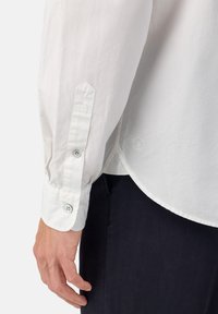 Witte katoenen shirt met lange mouwen, featuring knoopmanchetten, een afgeronde zoom en een subtiele logo-detail nabij de onderkant.