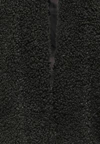Gros plan sur un tissu polaire noir texturé avec une ouverture verticale étroite révélant un tissu noir lisse en dessous.