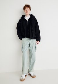 Black hooded jacket with multiple pockets, layered over a black top, paired with light blue cargo pants and sneakers featuring gray and white accents.