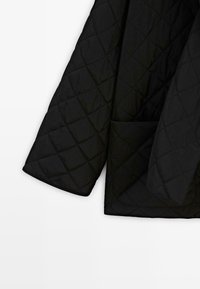 Black quilted fabric jacket sleeve and hem with diamond stitching and a patch pocket on a white background.
