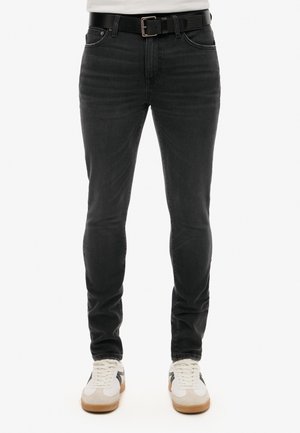 Black denim jeans with a slim fit, featuring five pockets, a leather belt, and subtle whiskering on the front. Worn with white sneakers.