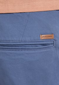 Modré látkové šortky s našitými kapsami a hnědou koženou štítkem s názvem "JACK & JONES" připevněným na pase.