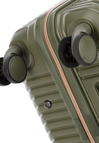 Ecken eines olivgrünen Hartschalenkoffers mit zwei drehbaren Rollen und einem roségoldenen Reißverschluss vor weißem Hintergrund.