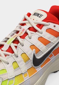 Αθλητικό παπούτσι Nike με λευκά κορδόνια, μαύρο λογότυπο και πολύχρωμες πλέξεις σε κόκκινους, πορτοκαλί και κίτρινους τόνους.