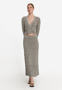 Grå stickad cardigan med djup V-ringning och tre knappar, kombinerad med en matchande lång kjol. Mjuk textur och figurnära siluett.