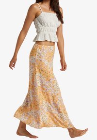 Top de peplum en tejido blanco texturizado, combinado con una falda maxi de estampado floral en naranja, con pequeños acentos en púrpura y verde.