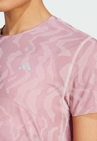 Camiseta deportiva rosa con un patrón geométrico y acentos de tonos claros. Mangas cortas y un cuello redondo con tejido texturizado.