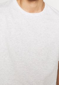 Lichtgrijze katoenen t-shirt met een ronde halslijn en korte mouwen. Zachte textuur, subtiel gemêleerd patroon en geen zichtbare logo's of graphics.