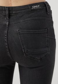 Sorte denimbukser med en tett design, som har en baklomme og merket "ONLY." Materialet har en glatt tekstur.