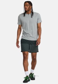 T-shirt en coton gris associé à un short noir avec des rayures vertes horizontales, complété par des chaussures noires et des chaussettes blanches.