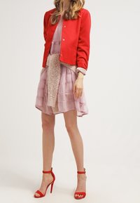 Czerwony krótki żakiet nałożony na jasnoróżową sukienkę w warstwy, z puszystą beżową częścią środkową. Uzupełniony czerwonymi sandałami na wysokim obcasie.