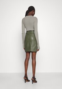 Grøn lædermininederdel med høj talje, glat tekstur og slids bagpå. Kombineret med en grå ribbet langærmet top.