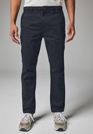 Schwarze Cargo-Hosen mit geradem Schnitt, ausgestattet mit Seitentaschen und einer glatten Stoffstruktur. Getragen mit hellbraunen und weißen Sportschuhen.