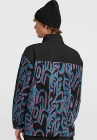 Veste en polaire avec une partie supérieure noire et une section inférieure à motif en bleu, rose et noir. Dotée d'un col haut et d'une coupe ample.