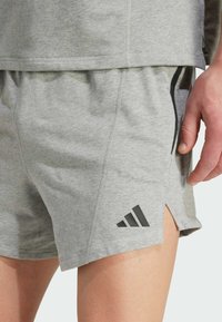 Shorts de sport gris en tissu doux, arborant un logo adidas noir, des aérations latérales et une taille confortable. La texture est lisse et respirante.