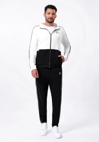 Zwart-wit zip-up sport tracksuit met een half-zip ontwerp, gestreepte accenten en logo detail. Gepaard met witte sneakers.