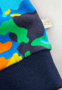 Polsino di felpa multicolore con un vivace motivo in arancione, verde, blu e nero. La texture a costine contrasta con il tessuto liscio.