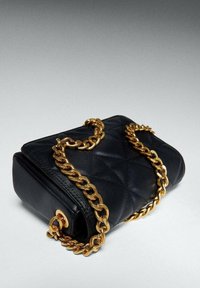 Czarna skórzana torebka z pikowanym wzorem, z złotym łańcuchem jako paskiem i okrągłym elementem dekoracyjnym. Prostokątny kształt o gładkiej fakturze.