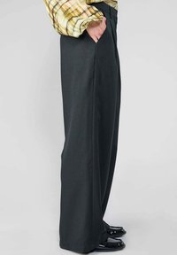 Schwarze, weit geschnittene Hosen mit vertikaler Rippstruktur, ausgestattet mit seitlichen Taschen und einem enganliegenden Bund, kombiniert mit einem karierten Oberteil in Gelb und Braun.