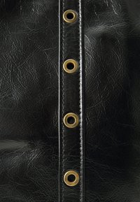 Närbild av svart läder med vertikal söm och fyra mässingsöglor jämnt fördelade längs sömmen.