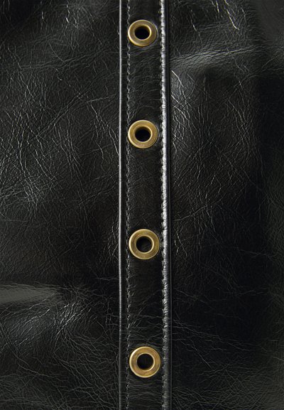 Gros plan d'un tissu en cuir noir avec une couture verticale et quatre œillets en laiton uniformément espacés le long de la couture.