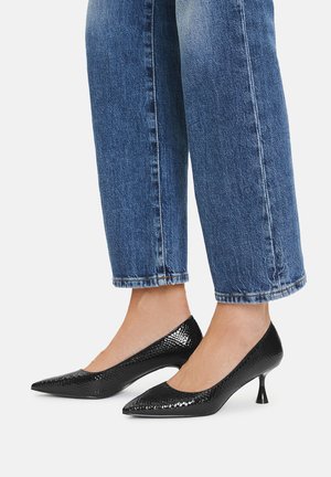 Czarne lakierowane czółenka z ostrym noskiem, fakturowaną powierzchnią i zwężającym się obcasem, połączone z dżinsami typu cuffed w niebieskim kolorze.