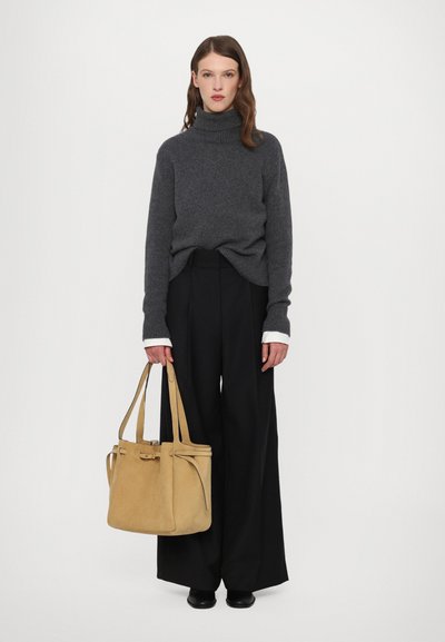 Grijze gebreide turtleneck trui, zwarte wijde broek, een tan suède schoudertas met dubbele handvatten en minimale details in de hand.