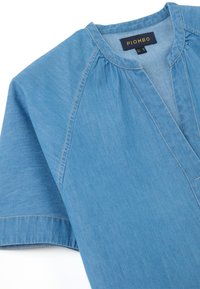 Camicia in denim azzurro chiaro con vestibilità rilassata, caratterizzata da un colletto a V, maniche corte e una consistenza morbida. L'etichetta nel colletto riporta la scritta "PIOMBO."