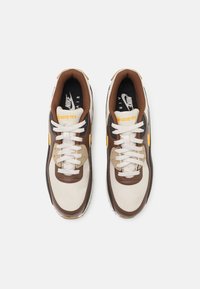 Tenisky Nike Air s béžovo-hnedou farebnou paletou, Gore-Tex materiálom, textúrovanými prekrytmi, tradičnými šnúrkami a okrúhlou špicou.