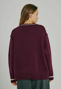 Bordó kötött pulóver bordás aljjal, texturált mintával és kontrasztos fehér varrással a nyaknál és az ujjaknál.