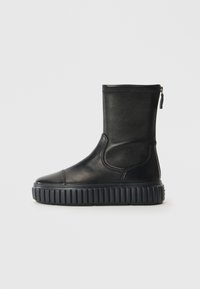Botte chelsea en cuir noir avec un bout rond, une semelle crantée et une fermeture éclair sur le côté. Sa texture lisse et son design minimaliste mettent en valeur son esthétique moderne.