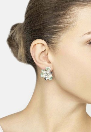 Silver flower-shaped earrings with green and clear gemstone accents. Floral design featuring curved petals and a shiny finish.