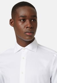 Balta pogu krekla ar klasisku apkakli, gludu tekstūru un šauru piegriezumu. Iespējami gaiši pogas un kārtīgi izgludināta izskats.