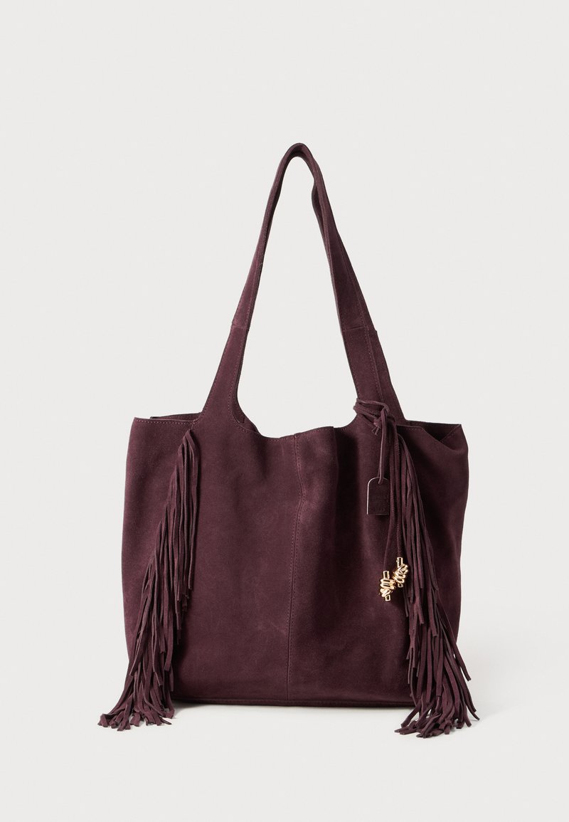 Burgundy suede tote bag with long fringe details, dual shoulder straps, and a decorative charm attached to the front.